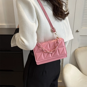 Sac à bandoulière rose matelassé avec chaîne acrylique porté par un mannequin en intérieur