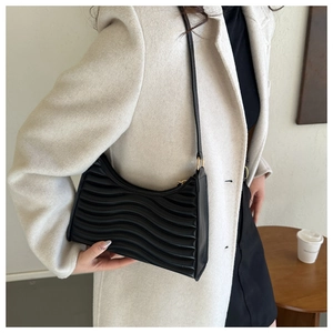 Detail of black wavy pleated baguette bag with golden metal hardware and long strap