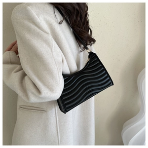 Detail of black underarm bag featuring unique horizontal wavy pleated texture and gold zipper