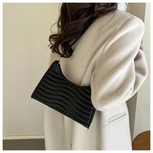 Detail of black pleated shoulder bag with wave texture worn with a beige wool coat
