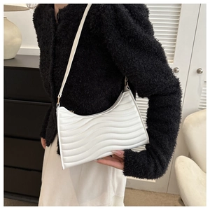 Detail of white wave-quilted shoulder bag with gold hardware worn by a model