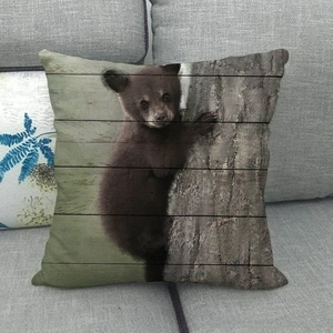 Linen throw pillow cover with bear cub climbing a tree on a vintage wood texture background