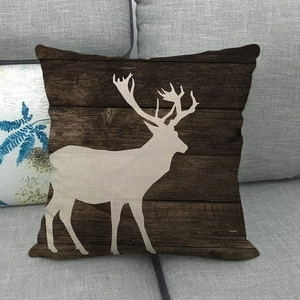 Détail de la housse de coussin en lin avec silhouette d'élan blanc sur fond grain de bois