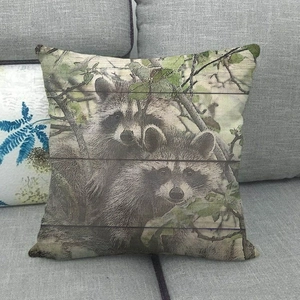 Linen pillowcase with raccoon design on wood grain background shown on a grey fabric sofa