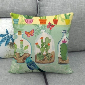 Linen decorative throw pillow cover with green birds and botanical plant prints on a gray sofa