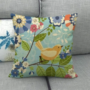 Detail of linen pillow cover with yellow bird and floral pattern on a grey sofa