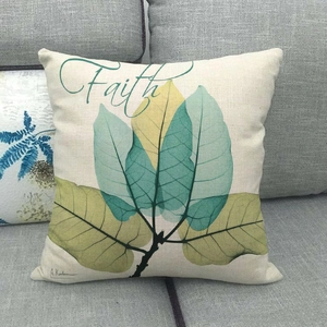 Détail du coussin en lin avec imprimé feuilles et texte Faith sur un canapé gris