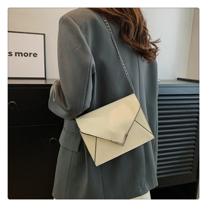 Chic cream leather envelope crossbody bag with V-shaped metal buckle on a shoulder