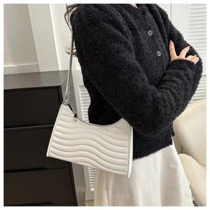 Elegant white shoulder bag with wave pattern quilting worn by a model in a minimal room
