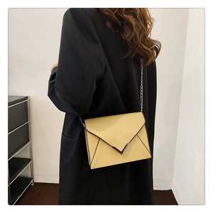 Close-up of light yellow envelope bag with V-shaped silver buckle and metal chain strap