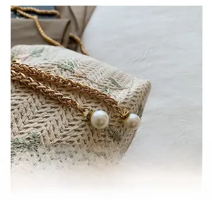Detailed close-up of the elegant pearl pendants and golden chain on a floral woven bag