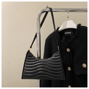 Close-up of black underarm bag featuring wave pattern texture and gold metal hardware