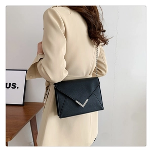 Detail of black envelope crossbody bag with silver V-shaped metal buckle and chain strap