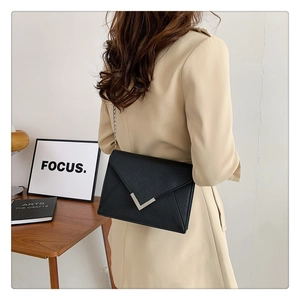 Detail of a black leather envelope bag with silver V-logo worn over a beige trench coat