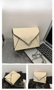 Detail of beige envelope crossbody bag featuring a silver V-shaped metal accent and chain