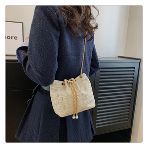 Detail of beige woven bucket bag with floral embroidery, gold chain, and pearl charms