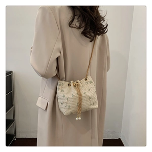 Detail of beige woven bucket bag featuring floral embroidery and gold chain strap