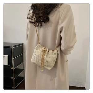 Detail of cream bucket bag with green floral pattern, gold chain, and pearl drawstrings