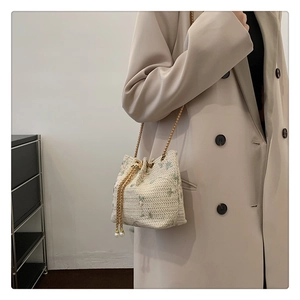 Detail of cream woven bucket bag featuring floral embroidery and large pearl drawstring