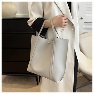 Detailed view of grey faux leather tote bag with gold magnetic clasp on white suit