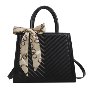 Quilted black leather tote bag with elegant patterned silk scarf on handle and shoulder strap