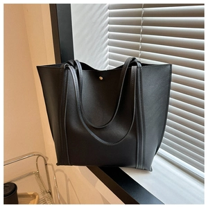 Detail of black faux leather tote bag showing fine stitching and gold snap button closure