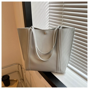 Detail of light gray tote bag featuring reinforced vertical stitching and a gold metal snap button