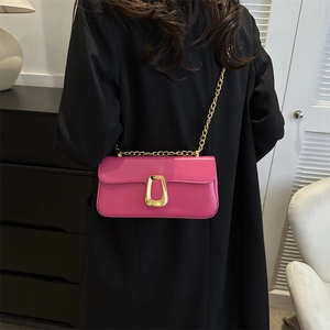 Pink minimalist chain crossbody bag with gold U-shaped buckle on black coat backdrop
