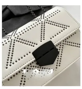 Close-up of white crossbody bag with round metal rivets and matte black geometric buckle lock