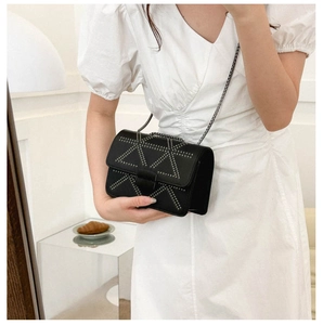 Detail of black crossbody bag with silver rivet pattern and metal chain on white dress