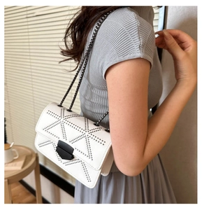 Detail of white crossbody bag with black metal rivets and dark grey chain strap