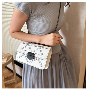 Detail of white crossbody bag with black rivet geometric patterns and metal chain strap
