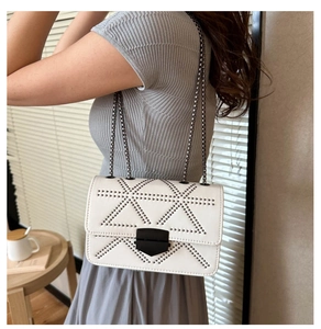 Close-up of white crossbody bag featuring black rivet triangle patterns and chain strap