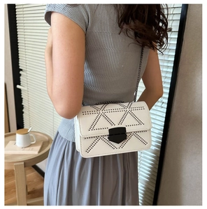 White crossbody bag with chain strap and rivet geometric patterns shown on a model