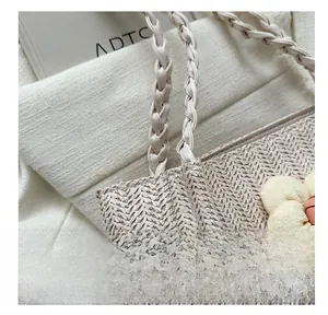Detailed close-up of ivory woven tote bag featuring floral charm and braided handle