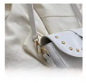 Gros plan sur les crochets dorés et rivets d'un sac besace blanc minimaliste
