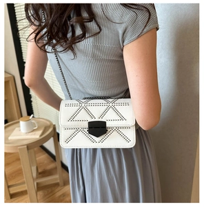 Detail of white crossbody bag with black rivets and metal chain strap in lifestyle setting