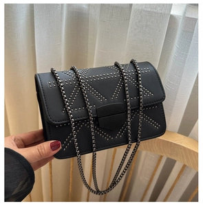 Detail of black crossbody bag with geometric rivet patterns and dark grey chain strap