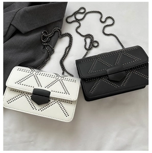 Detailed view of white and black crossbody bags with rivet triangles and metal chains