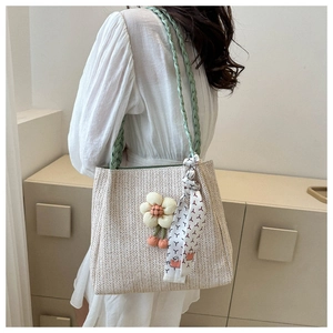 Detail of straw tote bag with green straps floral pendant and silk scarf accent