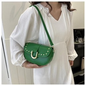 Détail du sac selle vert avec rivets dorés et boucle magnétique en U sur robe blanche