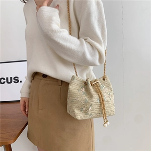 Beige woven bucket bag with floral embroidery, gold chain strap and pearl drawstring detail