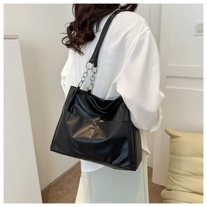Detail of black PU leather tote bag with silver chain strap shown on a model