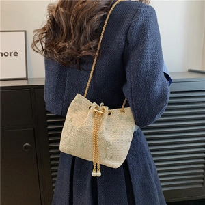 Chic cream bucket bag with floral embroidery and gold chain strap shown on model