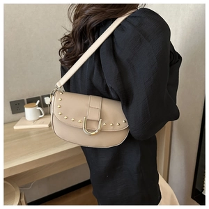 Détail du sac selle beige avec clous dorés et boucle en U porté par un mannequin