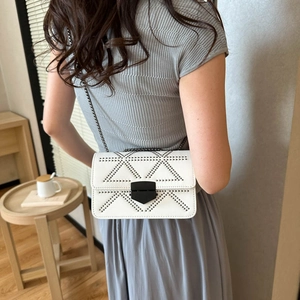 White minimalist chain crossbody bag with metal stud patterns worn by a model
