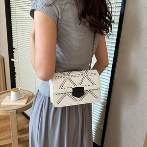 White minimalist crossbody bag with black rivets and chain strap worn by a model