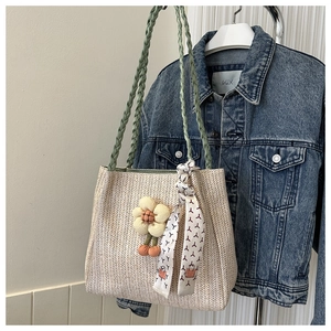 Detail of off-white woven tote with green handles, floral charm, and silk scarf