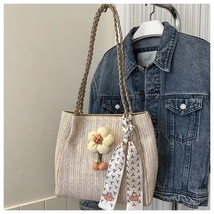 Detail of woven straw tote bag featuring a plush sunflower charm and printed silk scarf