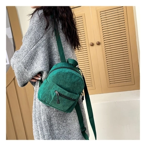 Detail of dark green corduroy backpack showing soft texture and compact design on model